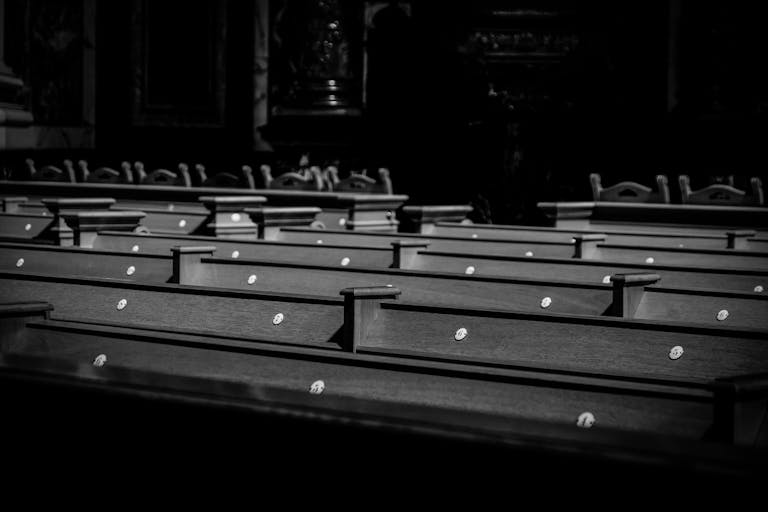 A serene black and white image of church pews in soft light, evoking a peaceful and contemplative atmosphere.