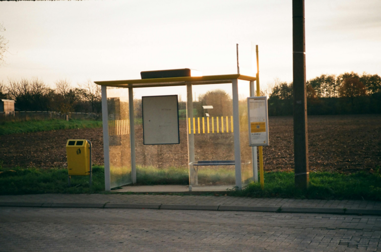 A serene countryside bus stop with glass walls at sunset, offering a tranquil view.